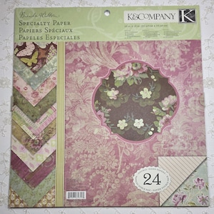 May include: A package of Brenda Walton Specialty Paper by K&Company. The paper is 12 in x 12 in (30.48cm x 30.48cm) and double-sided. The design features floral patterns in pink, green, and brown. The package includes 24 sheets.