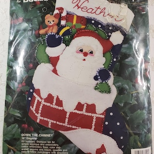 May include: A felt Christmas stocking kit featuring Santa Claus coming down the chimney with a teddy bear and presents. The kit includes stamped felt, embroidery floss, sequins, beads, needles, and instructions. The stocking is 15 inches diagonally. The kit is by Bucilla and says "Gallery of Stitches" and "Down the Chimney".