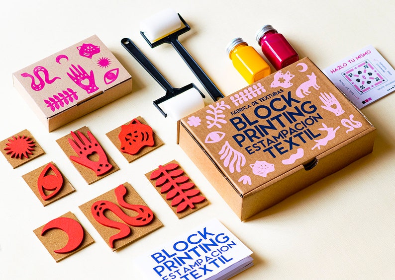 May include: A block printing kit with a brown box, pink and blue text, and a variety of red foam stamps. The kit includes two bottles of paint, one yellow and one red, and two black rollers.