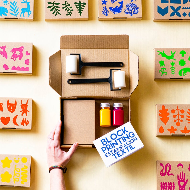 May include: A block printing kit containing two rollers, two bottles of paint, and a set of stencils. The stencils are in boxes with colourful designs. The kit includes instructions for block printing on fabric. The text on the card reads "Block Printing Estampacion Textil".