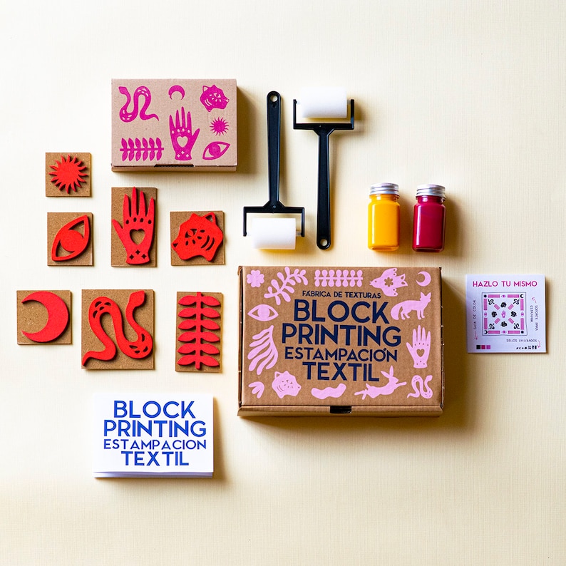 May include: A block printing kit with a variety of stamps, two bottles of paint, a roller, and instructions. The stamps feature designs such as a sun, eye, hand, snake, and leaves. The kit is labelled "Block Printing Estampacion Textil" and "Fabrica de Texturas".