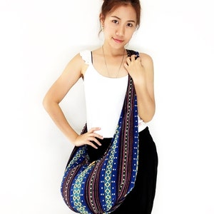 May include: A woman is wearing a white tank top and black pants. She is carrying a blue and yellow patterned shoulder bag with a long strap.