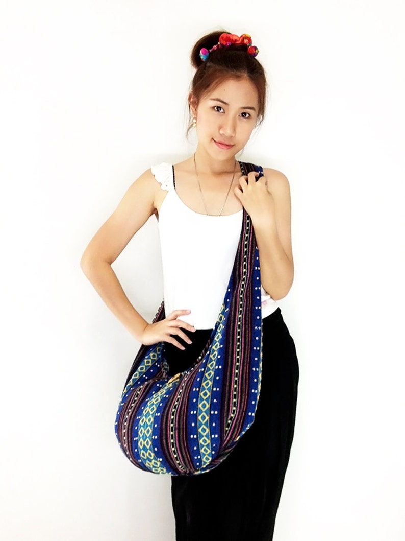 May include: A woman is wearing a white tank top and black pants. She is carrying a blue and yellow patterned shoulder bag with a long strap.