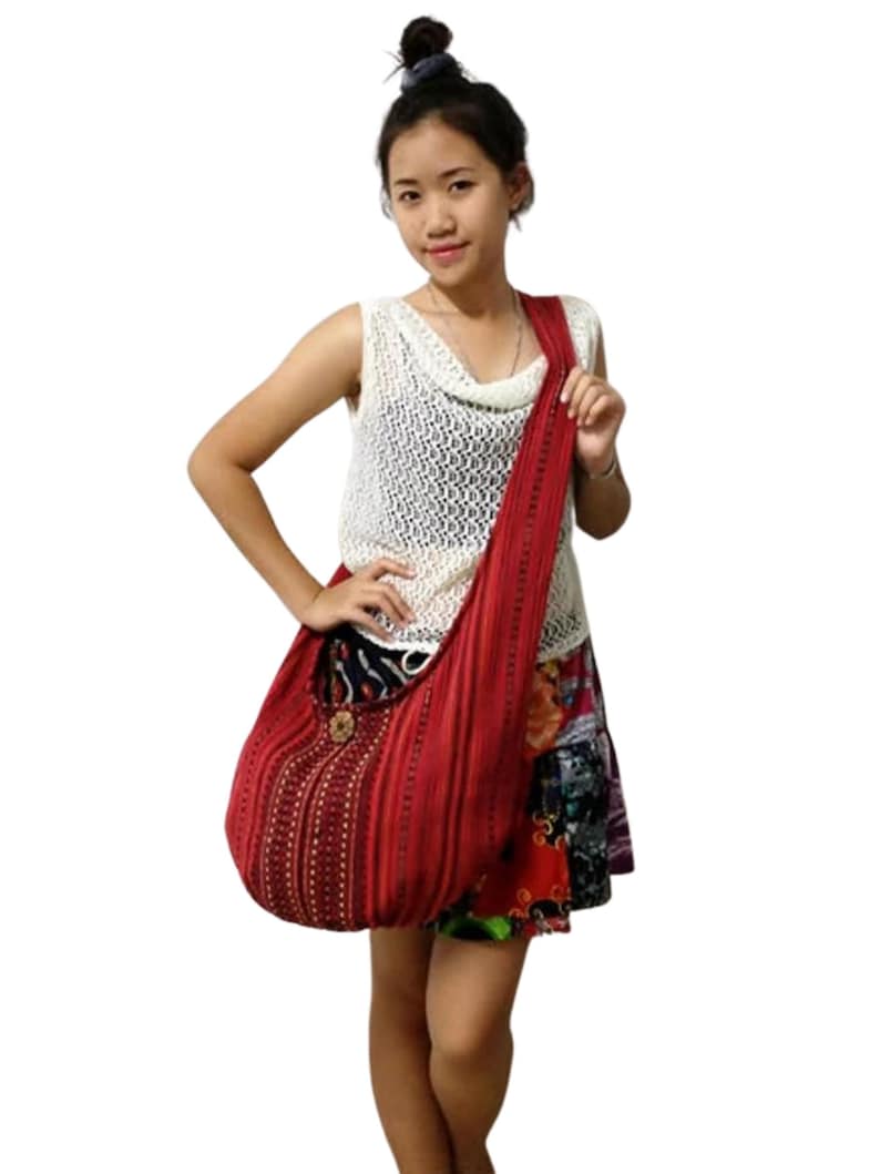 Pu&ograve; includere: Una borsa tote in tessuto rosso a righe con un bottone rotondo marrone e dettagli dorati. La borsa ha una tracolla lunga e viene indossata sulla spalla.