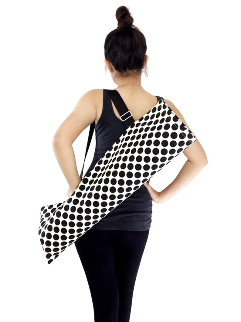 Puede incluir: Un porta-esterilla de yoga de lunares negros y blancos con una correa de hombro negra ajustable. El porta-esterilla est&aacute; hecho de lona y tiene una cremallera.