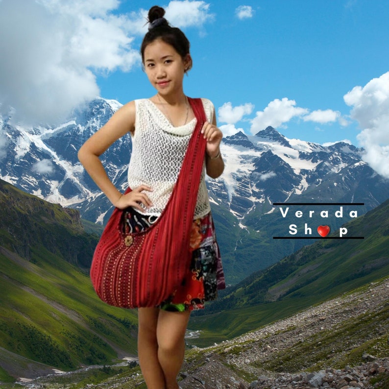 Pu&ograve; includere: Una borsa di stile hobo di colore rosso, realizzata a uncinetto, con una parte superiore in crochet bianco e dettagli marroni con perline. La borsa &egrave; indossata da una persona in piedi di fronte a una catena montuosa.