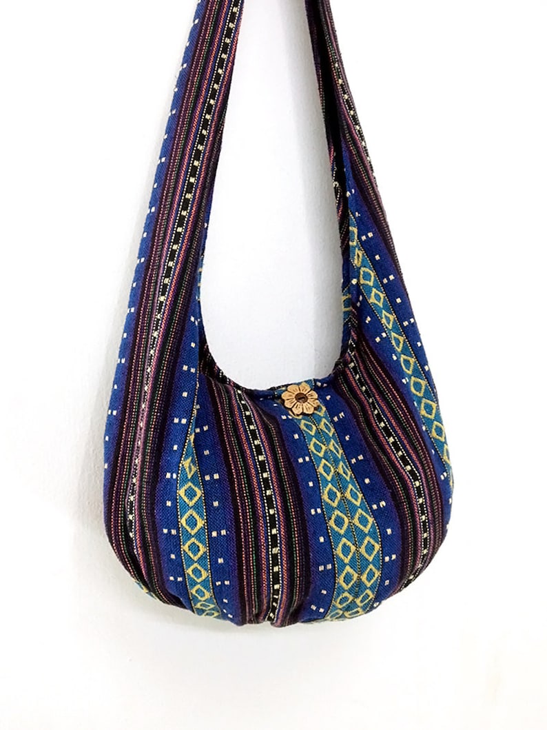 May include: A blue and yellow patterned hobo bag with a wooden button closure. The bag has a long strap and is made of woven fabric.