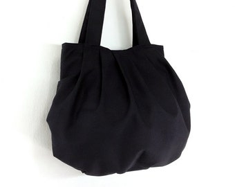 Puede incluir: Un bolso tote negro con un diseño fruncido y plisado. El bolso tiene dos asas largas.