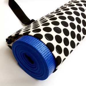 Puede incluir: Una esterilla de yoga azul enrollada dentro de una bolsa de transporte de lunares negros y blancos con una correa negra.