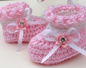 Puede incluir: Un par de botitas de bebé de crochet rosa y blanco con lazos de cinta de satén blanco y adornos de flores rosas.