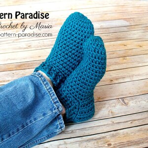 May include: A pair of teal blue crocheted slipper socks. The socks are worn on a person's feet, with the ankles showing blue jeans.
