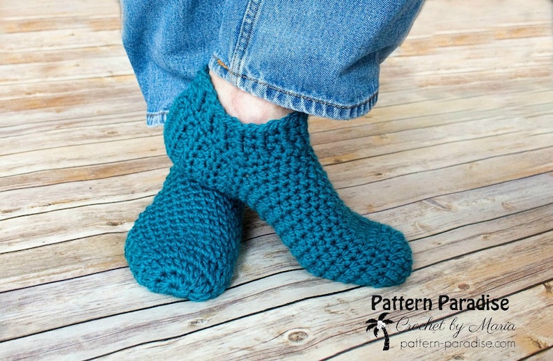 May include: A pair of teal blue crocheted slipper socks. The socks are worn on a person's feet. The socks are made with a simple stitch pattern.