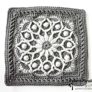 May include: A square, crocheted doily in shades of gray and white. The central design is a white floral pattern, surrounded by a gray border with a textured edge. The text "Pattern Paradise" is visible in the lower right corner.