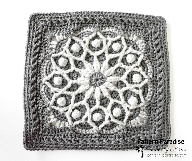 May include: A square, crocheted doily in shades of gray and white. The central design is a white floral pattern, surrounded by a gray border with a textured edge. The text "Pattern Paradise" is visible in the lower right corner.