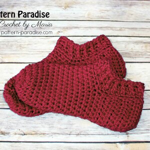 May include: A pair of crocheted burgundy socks on a wooden background. The socks are made with a simple stitch pattern and have a ribbed cuff.
