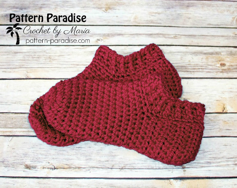 May include: A pair of crocheted burgundy socks on a wooden background. The socks are made with a simple stitch pattern and have a ribbed cuff.