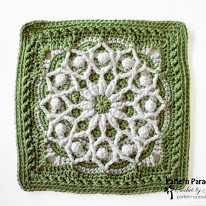 May include: A square, handmade crochet piece featuring a central floral design in white and light green, surrounded by a detailed border in a darker green. The piece has a textured appearance, with visible stitches and raised elements. The text "Pattern Paradise" is visible in the bottom right corner.