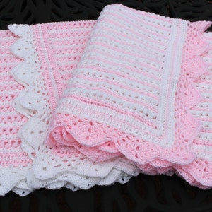 May include: A pink and white crocheted baby blanket with a scalloped edge. The blanket is made with a striped pattern and a delicate lace trim.