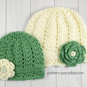 May include: Two crocheted hats with flowers. One hat is green and the other is cream. Both hats have a crocheted flower on the side. The text "pattern-paradise.com" is visible in the bottom right corner of the image.