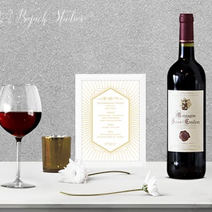 Puede incluir: Una tarjeta blanca con detalles dorados y un diseño geométrico. La tarjeta tiene el texto "Hearty's Recommended Drinks" y enumera diferentes tipos de bebidas. Un vaso de vino tinto, una botella de vino tinto y un portavelas dorado están sobre una superficie blanca.