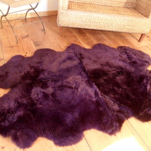May include: A deep purple sheepskin rug with a soft, fluffy texture. The rug is laid out on a wooden floor.