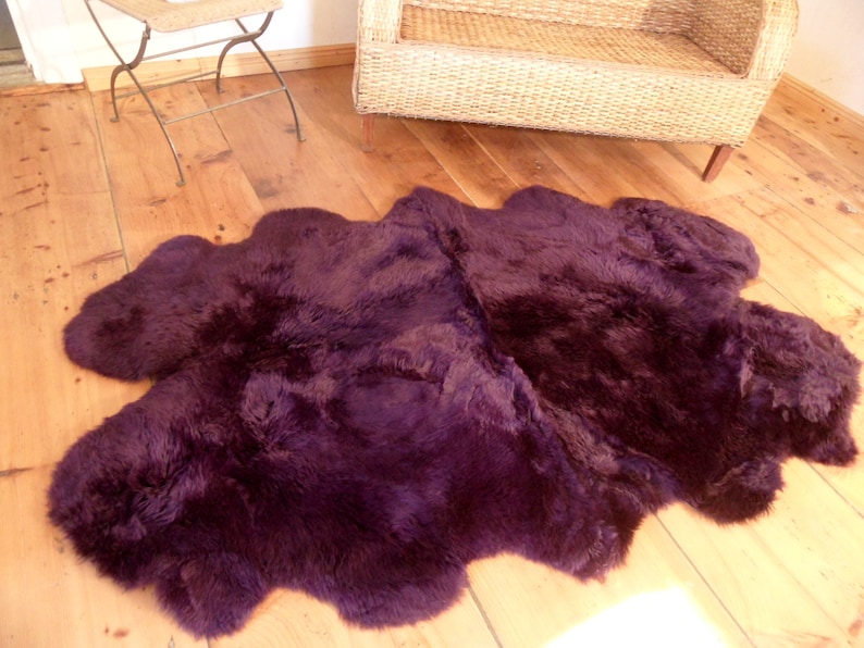 May include: A deep purple sheepskin rug with a soft, fluffy texture. The rug is laid out on a wooden floor.