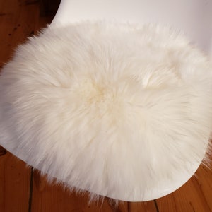 Könnte beinhalten: Weißer Kunstfell-Stuhlbezug. Das Kissen ist rund und flauschig und befindet sich auf einem weißen Stuhl.