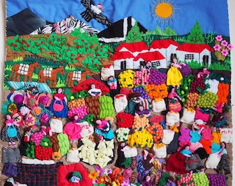 May include: A colorful fabric wall hanging featuring a detailed 3D applique scene of a bustling outdoor market. The landscape includes mountains, a bright yellow sun, and a bird in a blue sky above white houses and numerous figures selling produce.
