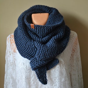 Peut inclure: Une écharpe en tricot bleu foncé avec une étiquette en cuir marron. L'écharpe est drapé autour d'un mannequin en dentelle blanche.