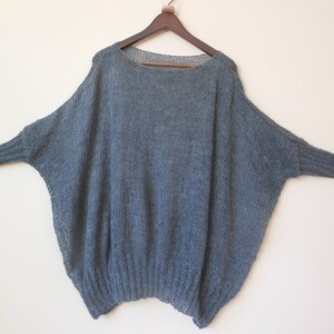 May include: A loose-fitting, gray knitted sweater with long sleeves and a wide neckline.