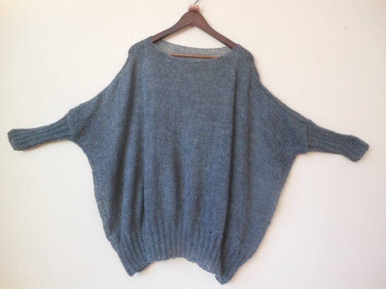 May include: A loose-fitting, gray knitted sweater with long sleeves and a wide neckline.