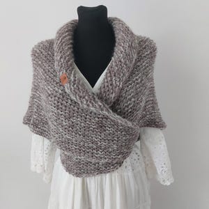 May include: A brown and white knitted shawl with a brown button. The shawl is draped over a white dress form.