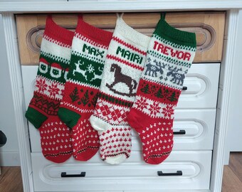 May include: Four Christmas stockings with personalized names, red and white patterned designs, and green accents. The stockings are hanging on a white dresser with wooden accents. The names include Max, Mairi, and Trevor.