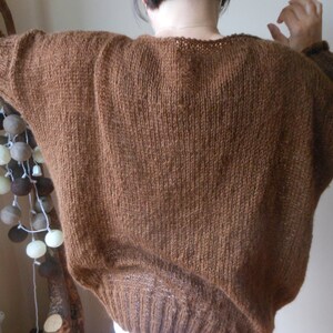 May include: A brown knitted sweater with a loose fit and a slightly dropped shoulder.