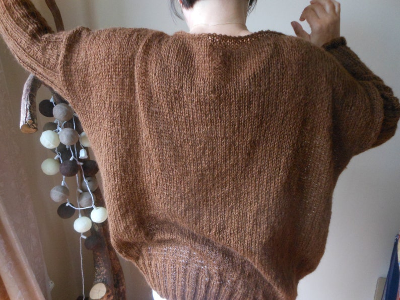 May include: A brown knitted sweater with a loose fit and a slightly dropped shoulder.