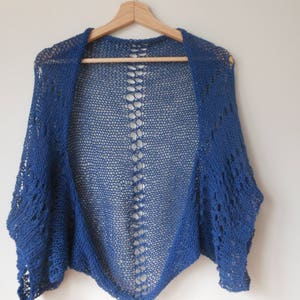 May include: A blue crocheted shrug with a lacy openwork design. The shrug is lightweight and has a relaxed fit.