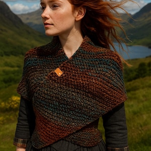 Peut inclure: Un châle tricoté marron, sarcelle et rouille, fixé avec un fermoir en cuir. Le châle est porté sur une robe gris foncé, avec un arrière-plan de montagne et de lac. Le modèle a les cheveux roux.