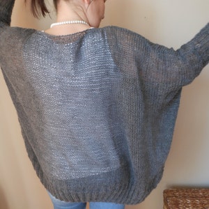 May include: A gray knitted cardigan with a loose fit and a wide neckline.