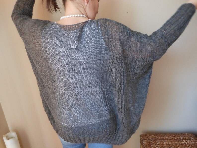 May include: A gray knitted cardigan with a loose fit and a wide neckline.