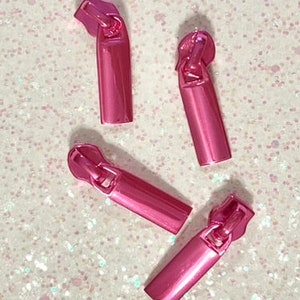 May include: Four pink metal zipper pulls. The pulls are rectangular and have a shiny finish.
