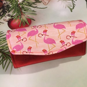 May include: A red leather wallet with a pink and white fabric flap featuring a pattern of pink flamingos wearing Santa hats and holding candy canes.