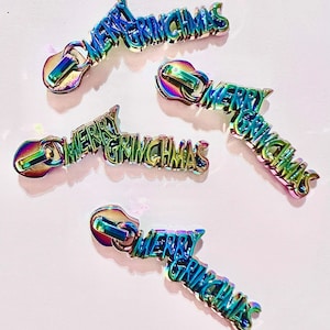 May include: Four iridescent zipper pulls with the text "Merry Grinchmas" in a rainbow color scheme.