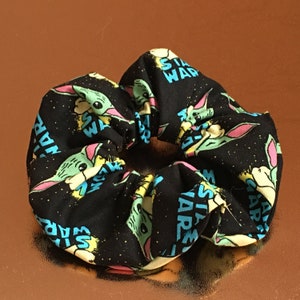 May include: Black scrunchie with a repeating pattern of a green alien character and the text "Star Wars" in blue and yellow.