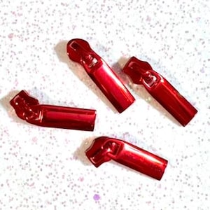 May include: Four red metal zipper pulls. The zipper pulls are shaped like a small, elongated cylinder with a rounded end.
