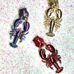 May include: Three lobster zipper pulls in different colors: iridescent purple, gold, and red. The lobster zipper pulls are a fun and unique way to add a touch of personality to your clothing or bags.