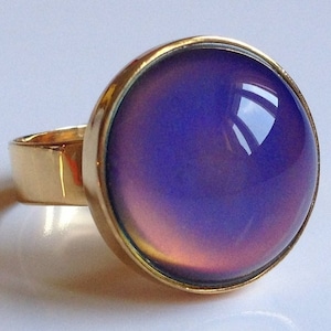 May include: A gold ring with a large, round, iridescent mood stone. The stone changes color depending on the light and temperature.