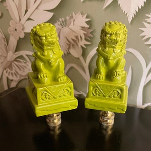 May include: Two green ceramic foo dog finials with gold accents. The foo dogs are sitting on square bases with intricate designs. The finials are approximately 4 inches tall.