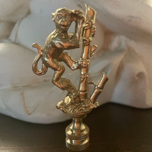 May include: A gold-toned metal lamp finial featuring a monkey figurine climbing a bamboo stalk.