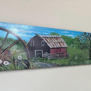 May include: A hand saw with a wooden handle and a painted landscape scene. The artwork depicts a barn, water wheel, trees, and a blue sky. The saw blade is painted with a rural scene, showcasing a rustic aesthetic.