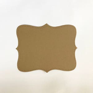 May include: A brown paper tag with a scalloped edge. The tag is blank and ready for writing.